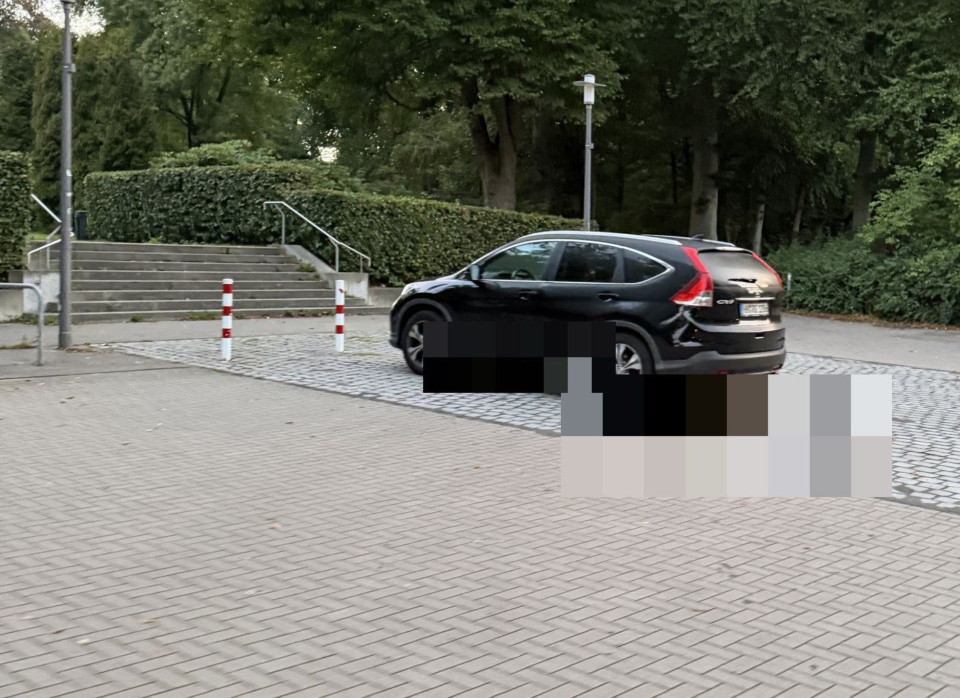 Auto quer auf dem Zufahrtsweg zwischen den Sperrpfosten vor der Treppe zum Park