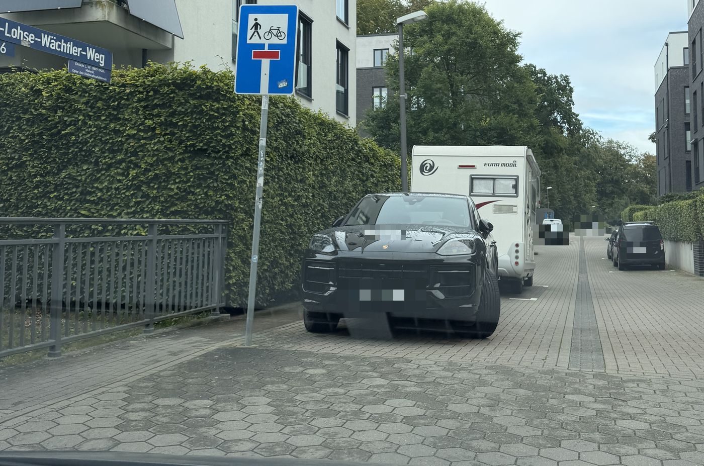 SUV quer vor der Hecke, in die Durchfahrt hineinragend